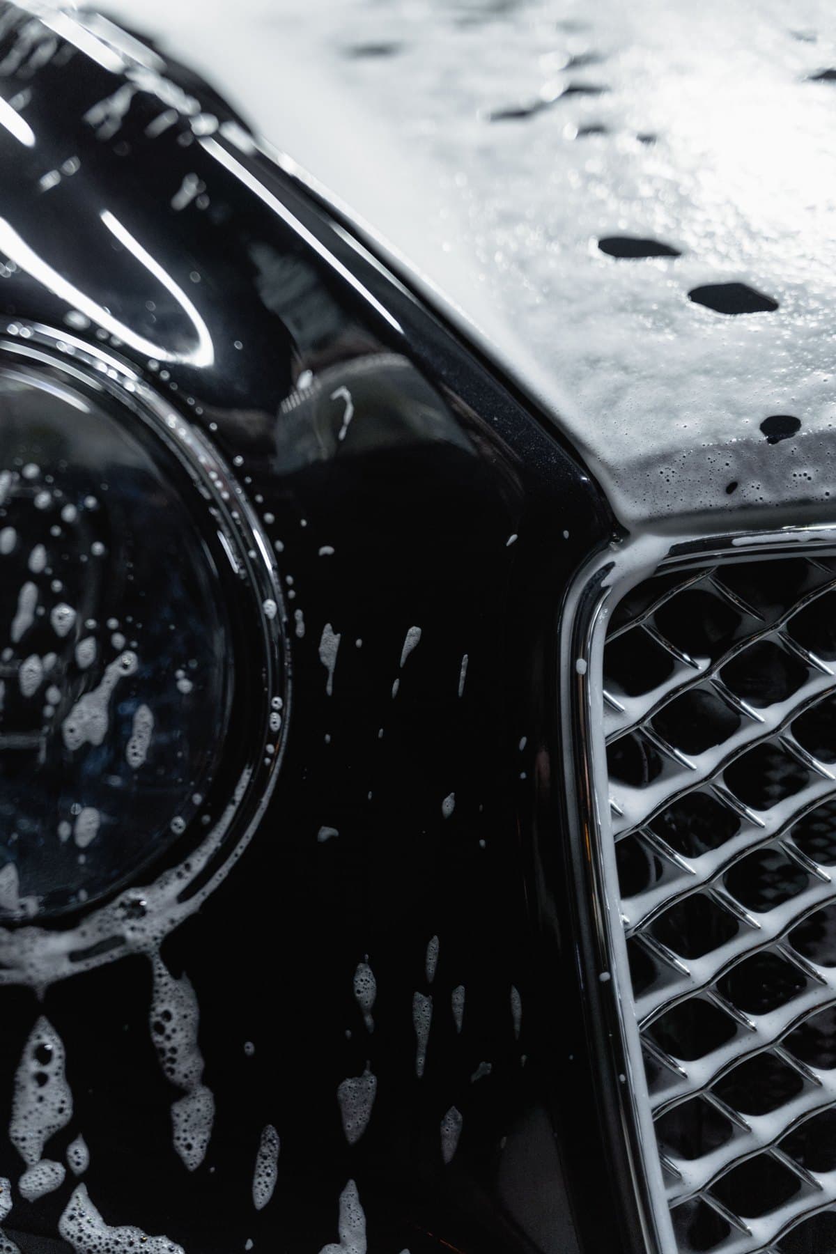 A black car covered in fresh foam during a premium hand wash, low-key studio light